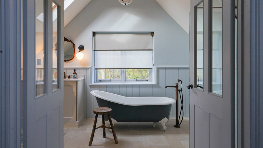 Cotswolds heritage bathroom featuring VENESTRE double roller blind with two fabrics, custom-fitted to original windows above a freestanding bathtub. The window treatments preserve architectural character while providing privacy and diffused natural light.