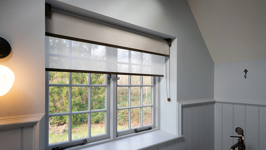 Close-up of VENESTRE made-to-measure roller blind in a heritage Cotswolds setting, installed on traditional mullioned windows. The custom window treatment features a soft, light-filtering fabric and antique bronze hardware, blending seamlessly with period details.