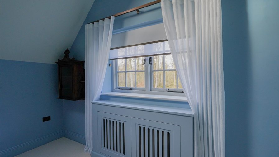 Cotswolds bedroom with VENESTRE bespoke roller blind and sheer curtains, fitted to original windows. The window treatments combine elegant fabrics and minimal hardware, enhancing the room’s heritage features while delivering modern comfort and style.