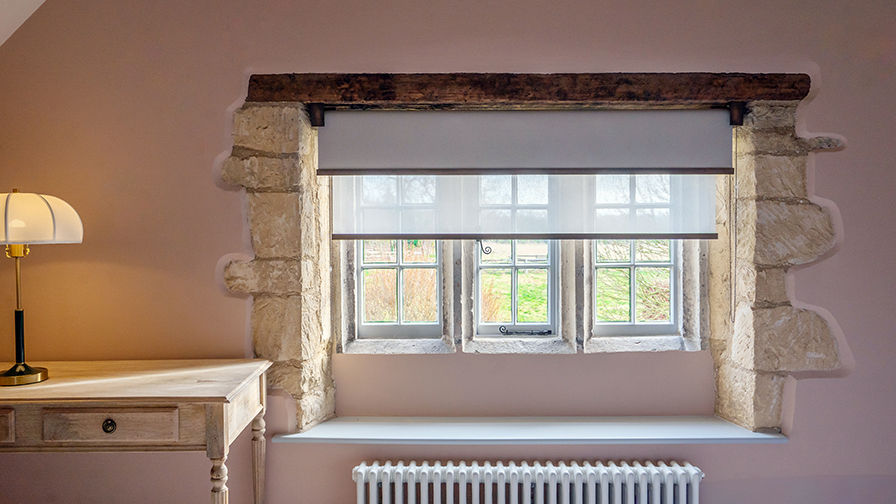Cotswolds heritage interior with VENESTRE bespoke roller blind in sheer fabric, fitted to original stone-mullioned windows. The custom window treatment preserves period details while enhancing privacy and natural light, reflecting VENESTRE’s expertise in luxury heritage window solutions.