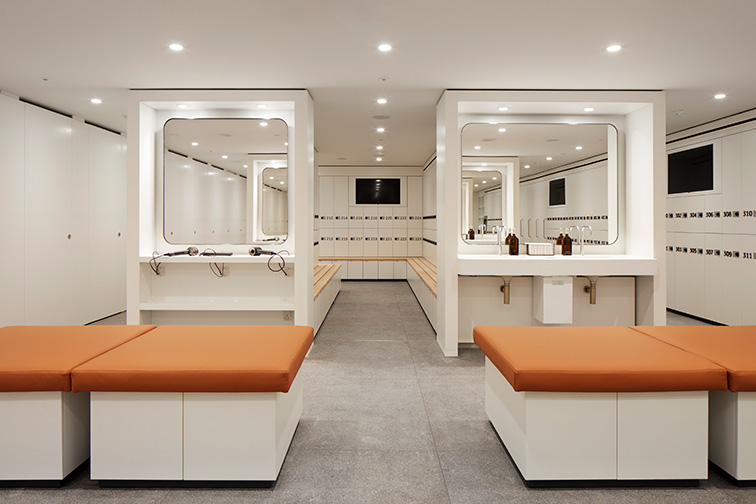 Large benches at the forefront of the image, two vanity stations and lockers that sit behind them at the back of the room