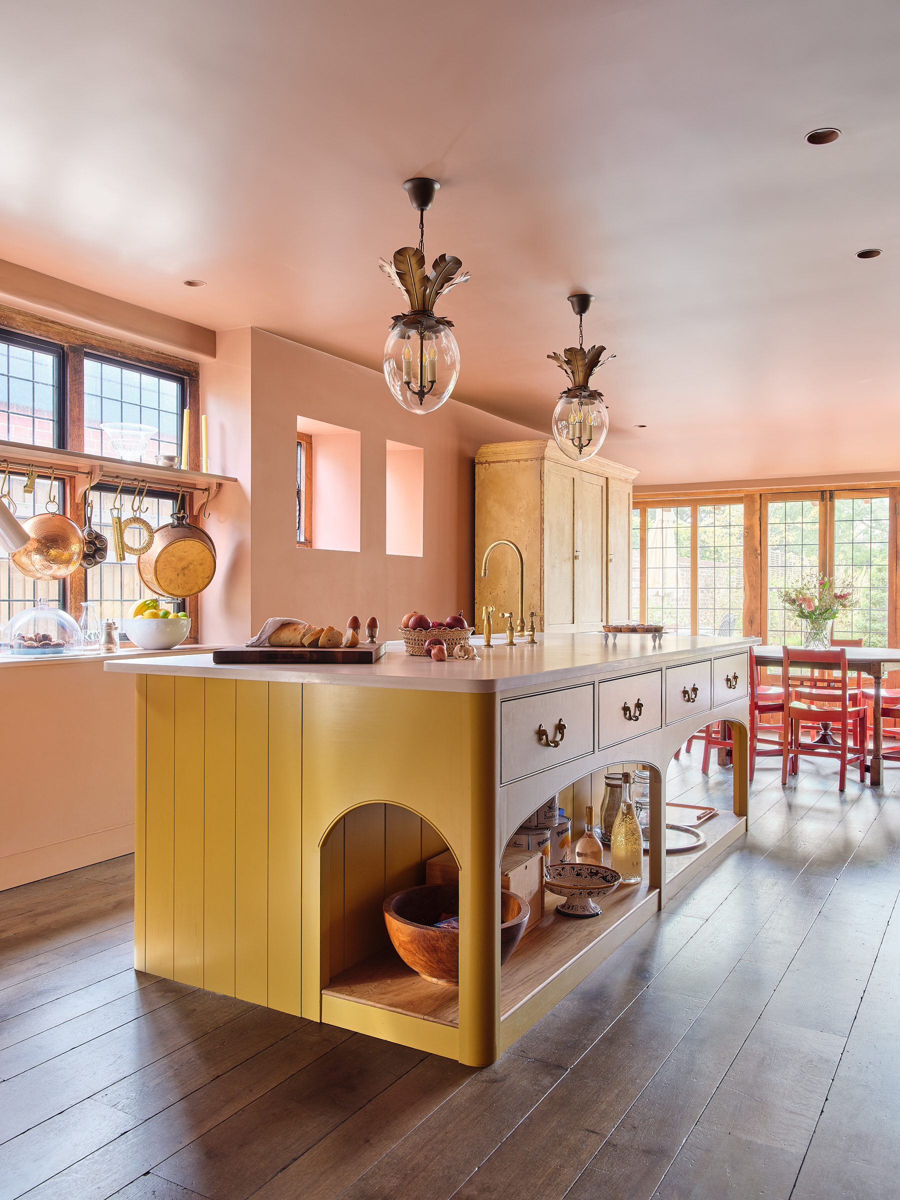 Pink and yellow Plain English kitchen with red accents and wide board oak floor