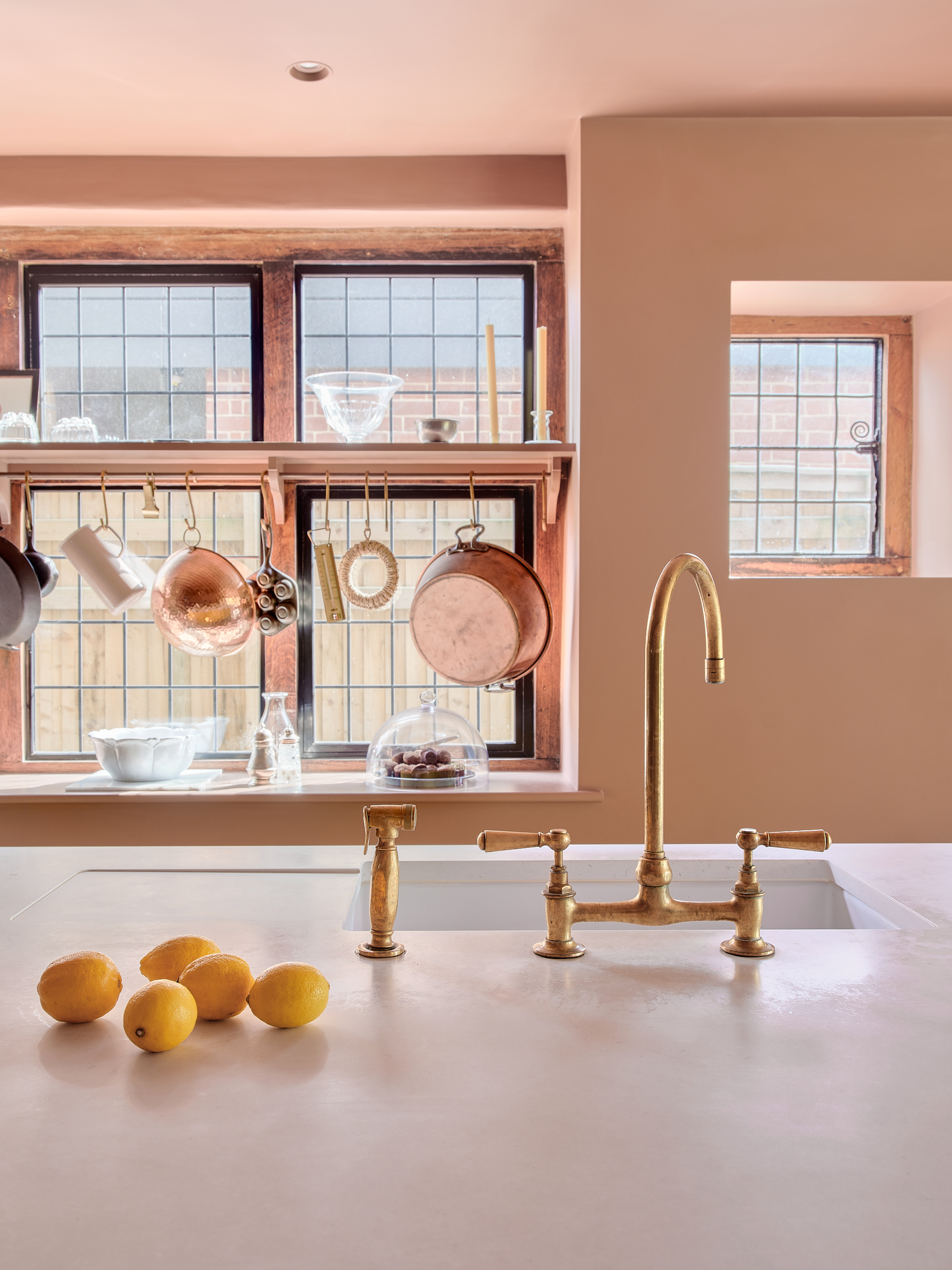 Copper Pans hung from brass rail added to window in Plain English kitchen in dusky pink