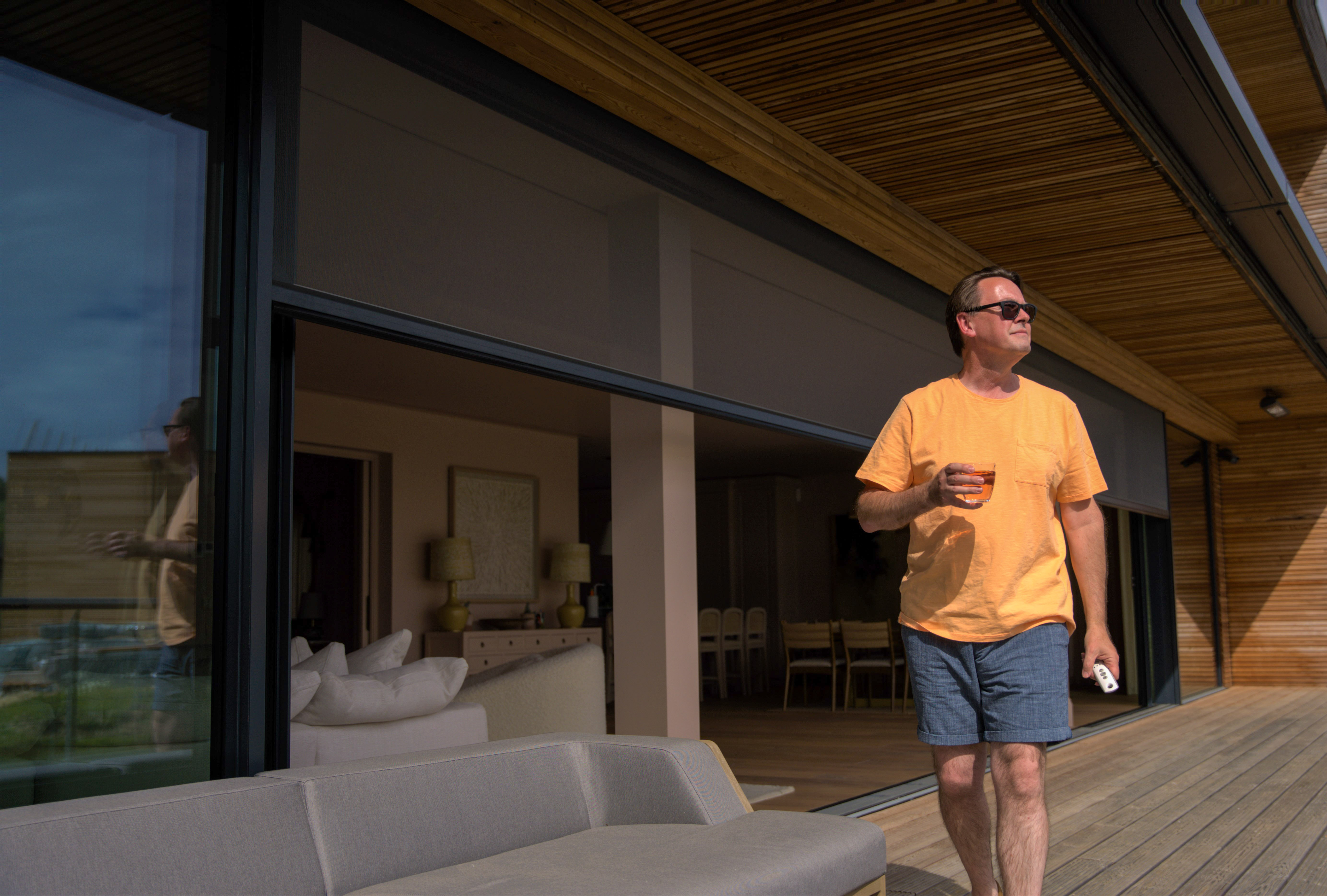 Man walking out of luxury lakeside property with motorised screen closing behind
