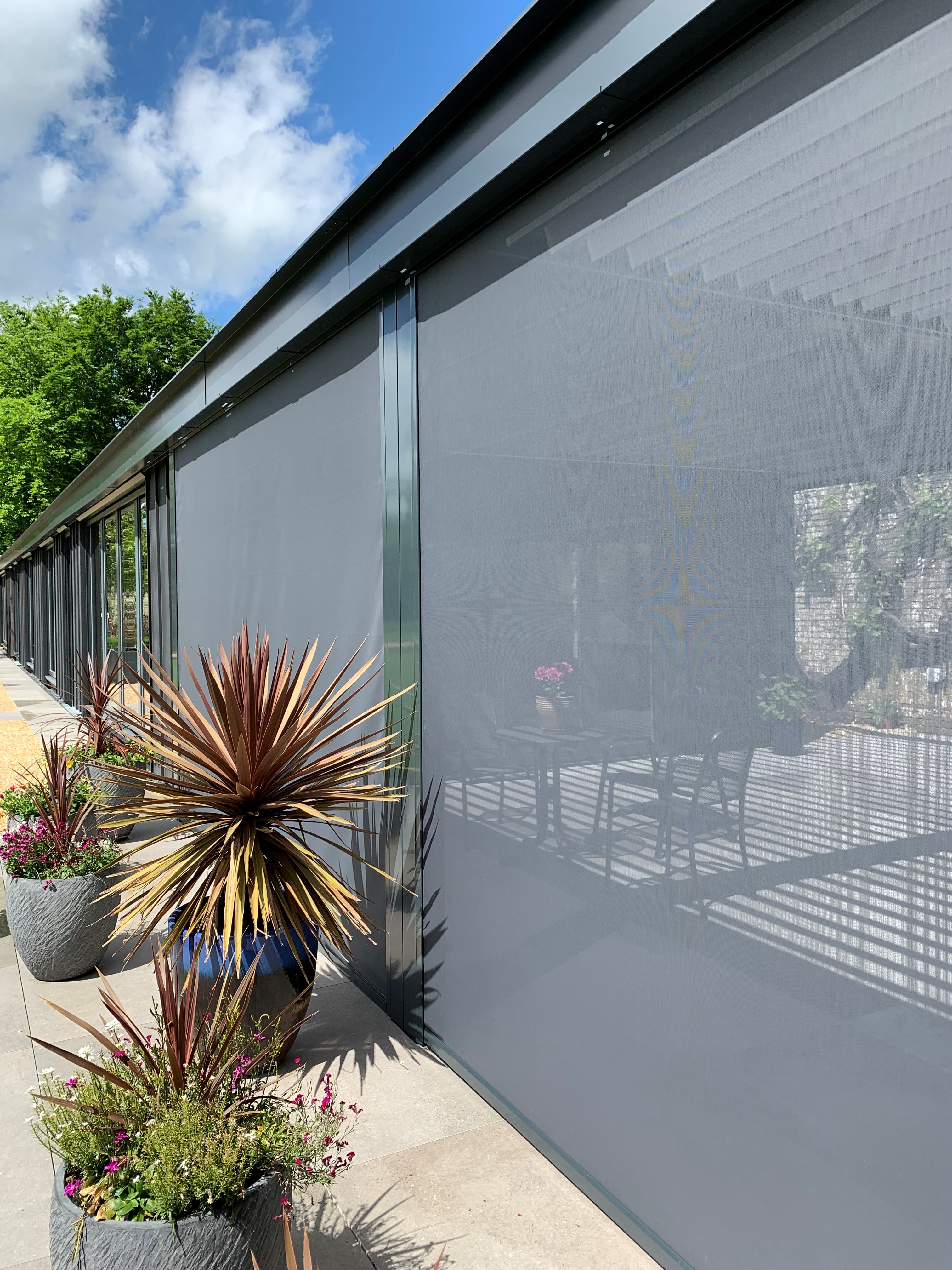 Power screens elegantly integrated into the pergola structure, blending with the garden’s classic design