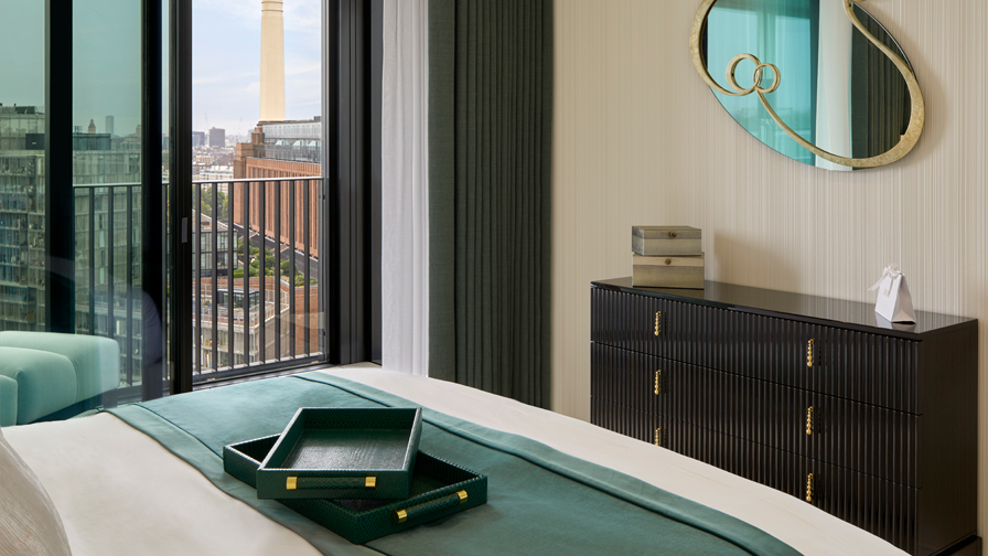 "Modern luxury bedroom with dark wood fluted dresser, sculptural gold mirror, green accent bedding with matching trays, and floor-to-ceiling glass doors overlooking city views