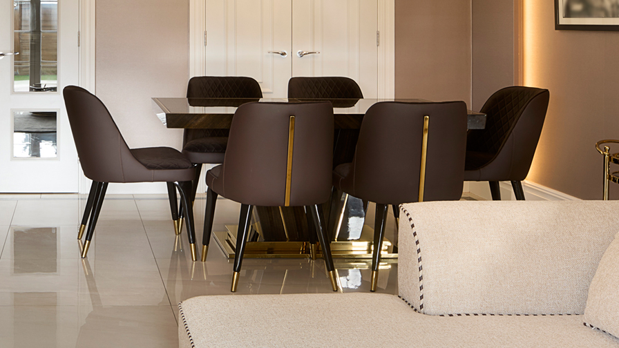 Elegant dining area with dark chocolate velvet dining chairs featuring gold accents, paired with a polished stone table and glossy tiled flooring in a luxury open-plan interior