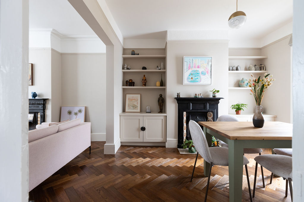 Lounge/dining room with parquet flooring, soft neutral walls & a pink sofa.