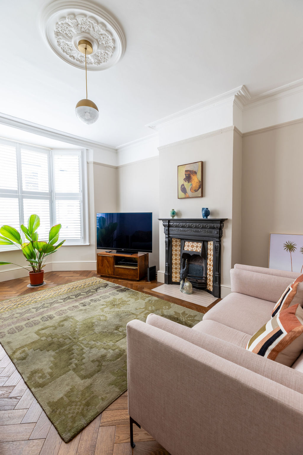Lounge decorated with warm neutral walls, parquet flooring with green rug and pink sofa.