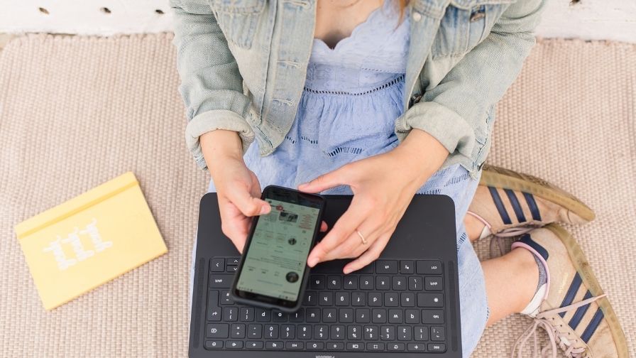 hands holding a mobile and a laptop.