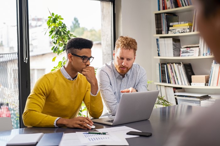 two people behind a desk looking at a laptop