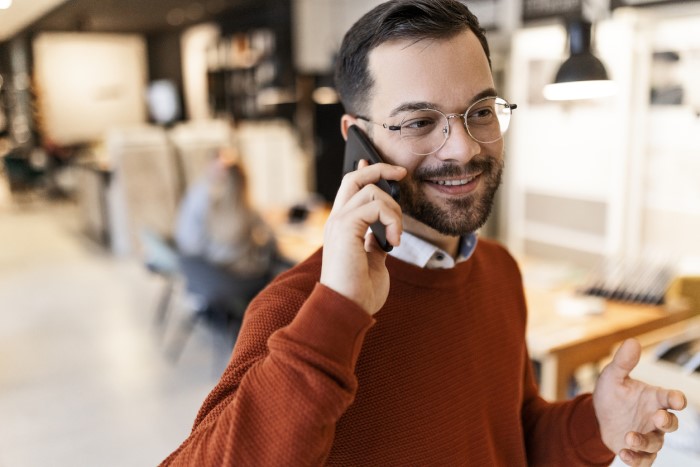 smiling man in a brown jumper talking on a mobile phone