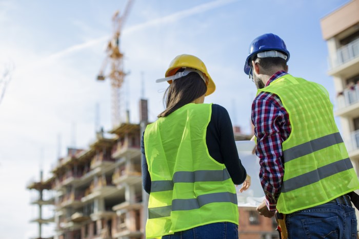 two people in high-vis jackets looking at a plan on a building site