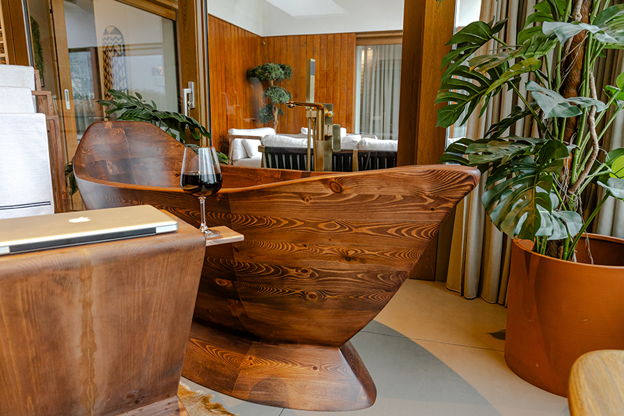 Front view of the Nautilus wooden bathtub styled for comfort, with candle, wine, and greenery, evoking the relaxed atmosphere of a modern homestead retreat.