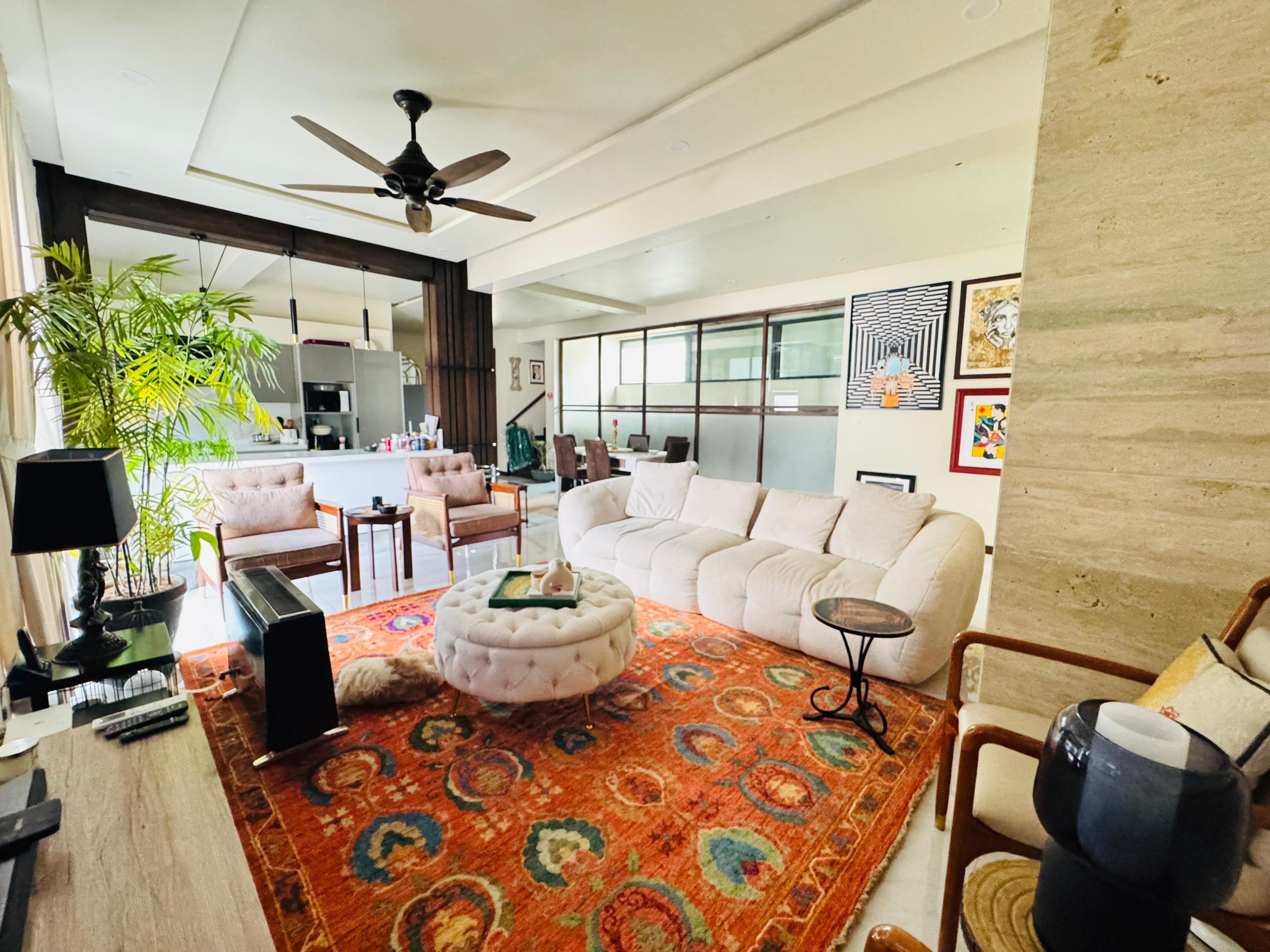 A contemporary, open-plan living room featuring a large, hand-knotted rug with a vibrant, orange-red Suzani floral pattern, placed under a white, curved sofa and ottoman.