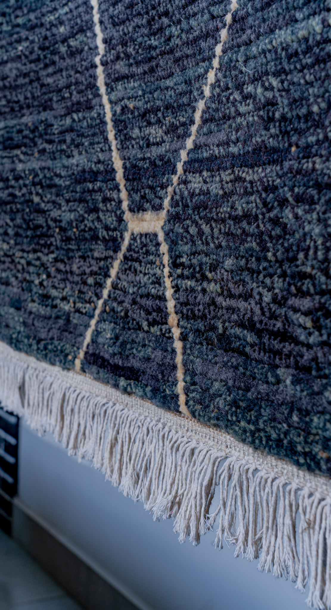 A closup hand-knotted, plush, Moroccan-style rug in a deep charcoal-blue, featuring a clean, geometric diamond-lattice pattern in a cream line, hung for display.
