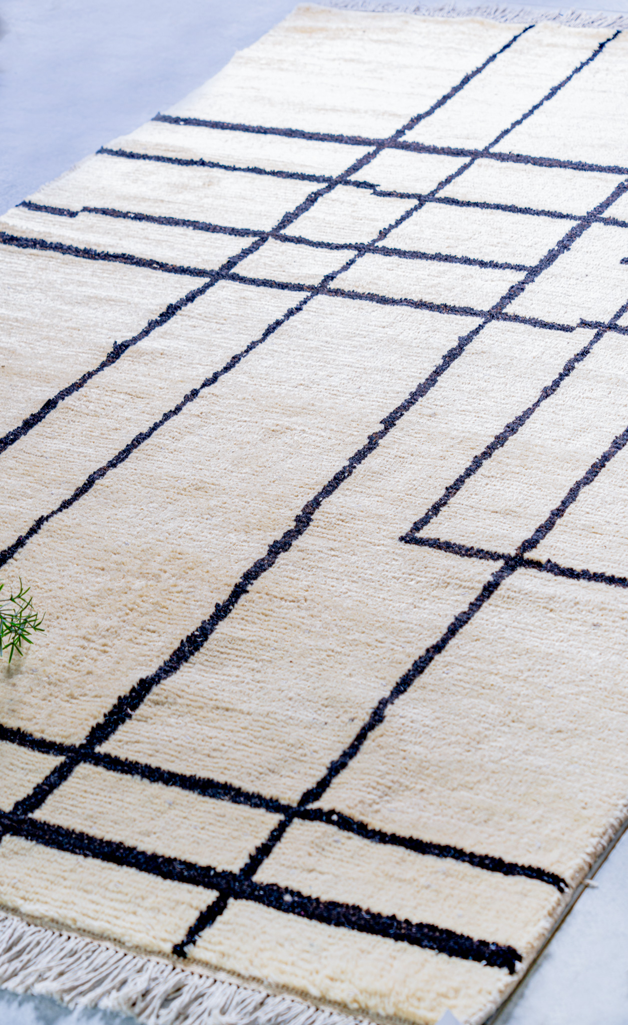 A close-up, angled view of a plush, hand-knotted, cream-coloured Moroccan-style rug, featuring a minimalist pattern of thin, intersecting, dark-brown lines.