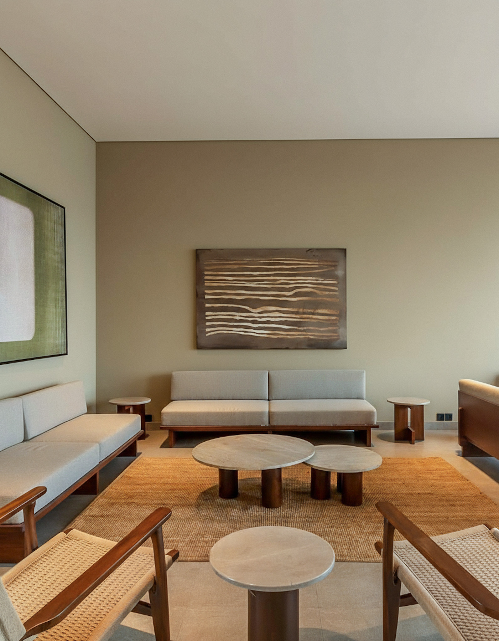 A contemporary resort lounge with minimalist grey sofas and wooden chairs set on a large, plain, natural-fibre jute rug, anchoring the seating area.