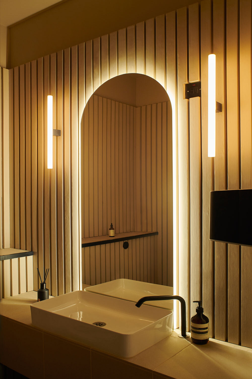 Large arched mirror with lighting behind on wooden wall