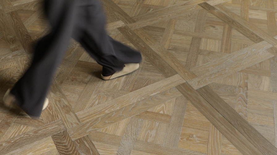 Topdown view of a Versailles panel floor with a person walking across in brown trousers.