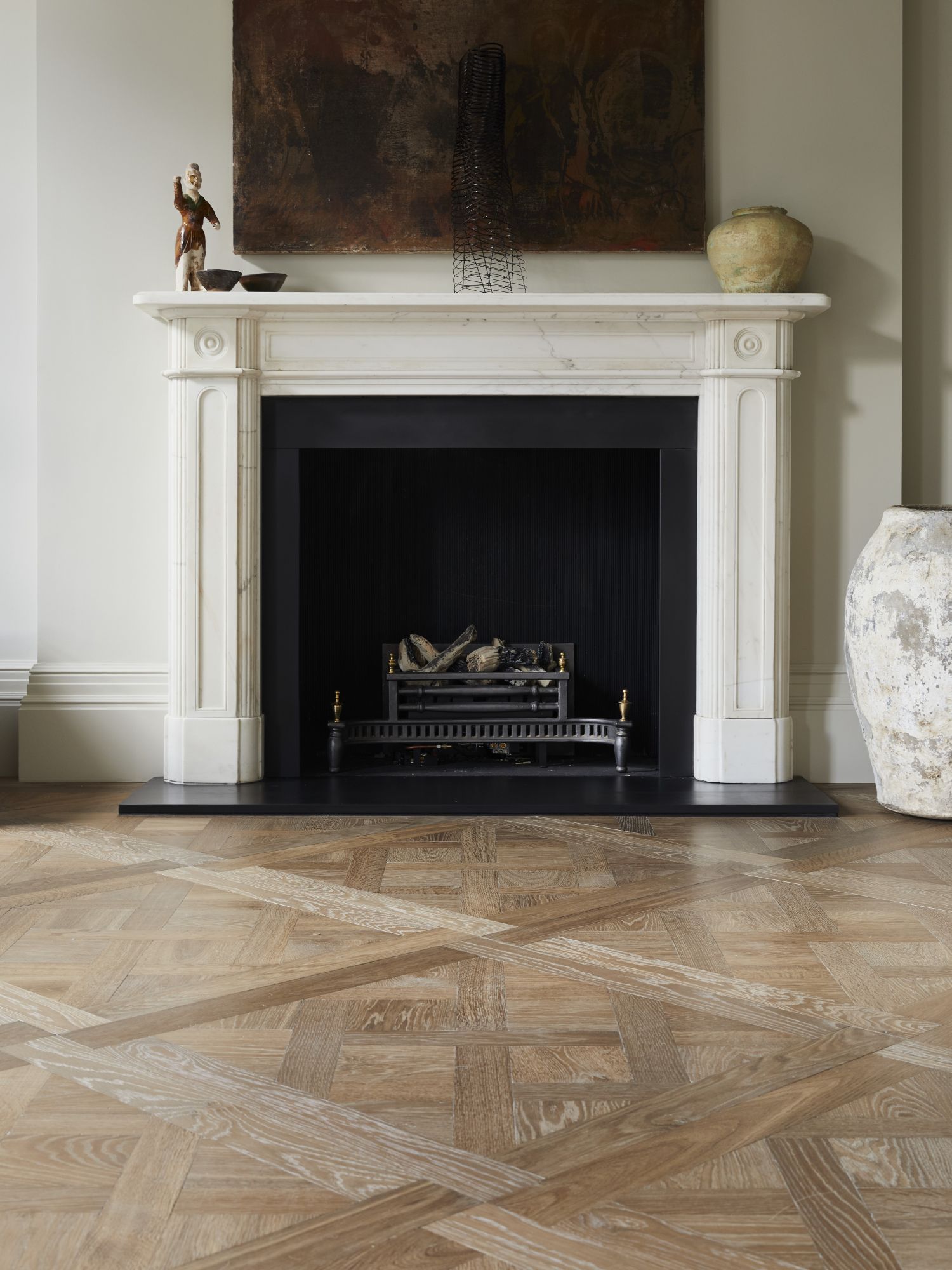A room with Versailles panel oak parquet and a restored Victorian fireplace with modern sculpture pieces and a painting above.
