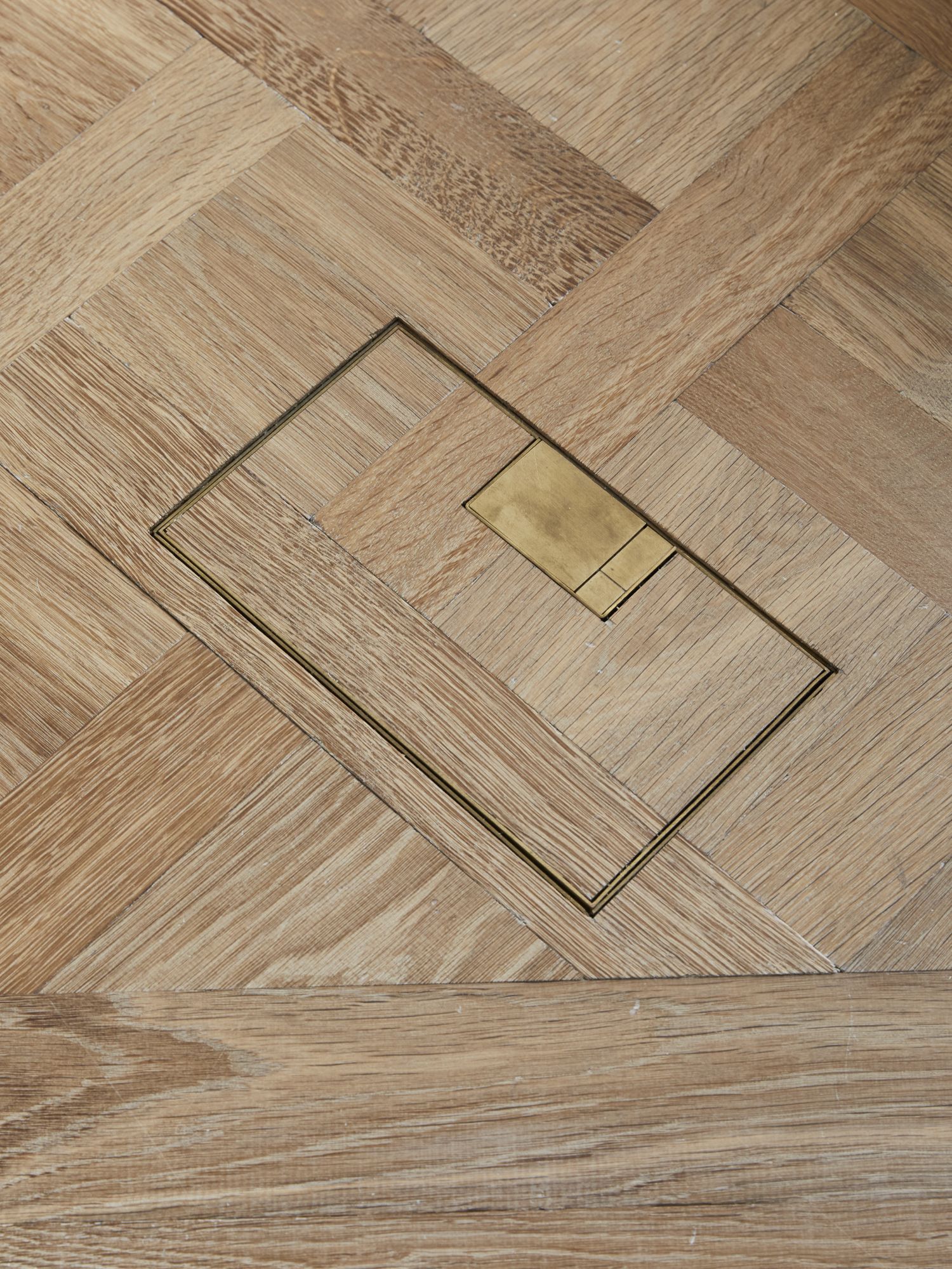 An electrical floor socket neatly installed within an oak Versailles panel parquet.