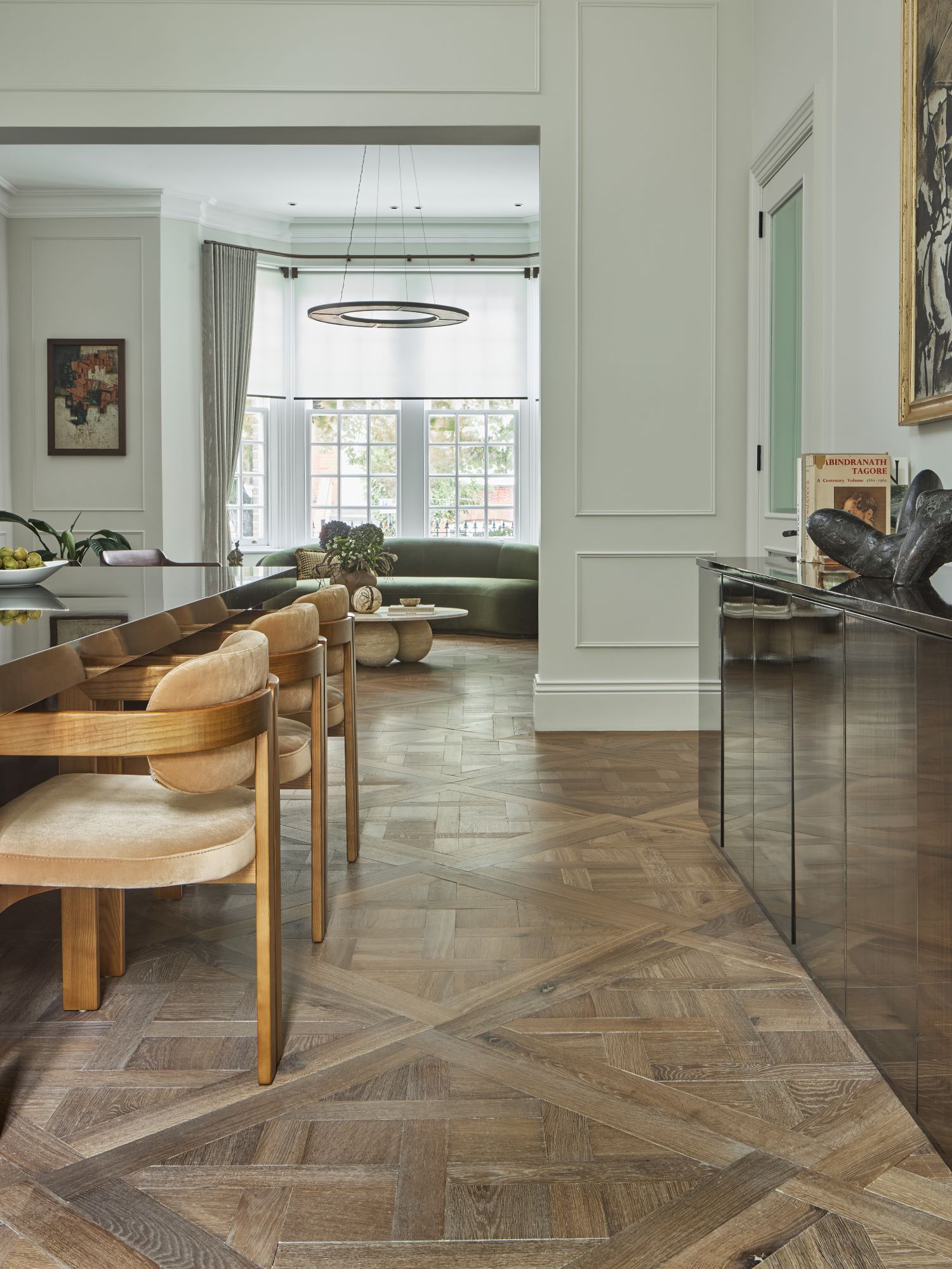 A view in a large reception room along the lenght wirh versailles flooring flowing throughout and with a dining area in the front and seating area in th back. 