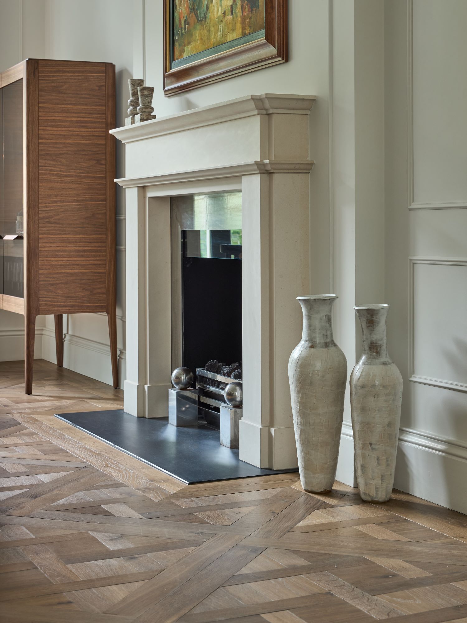 A restored white stone fireplace with black hearth and picture frame set in a Versailles parquet floor.