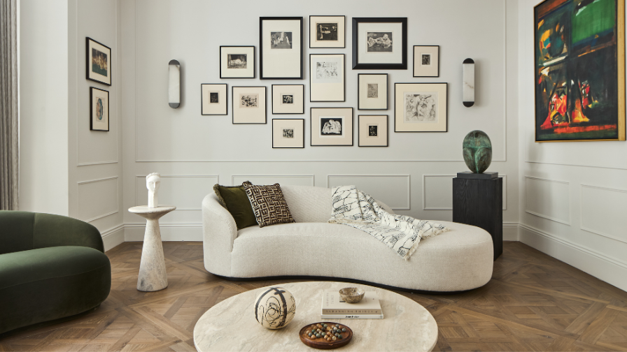 A view of a room with white walls and lots of small artwork with a white curved sofa flanked by sculptures. 