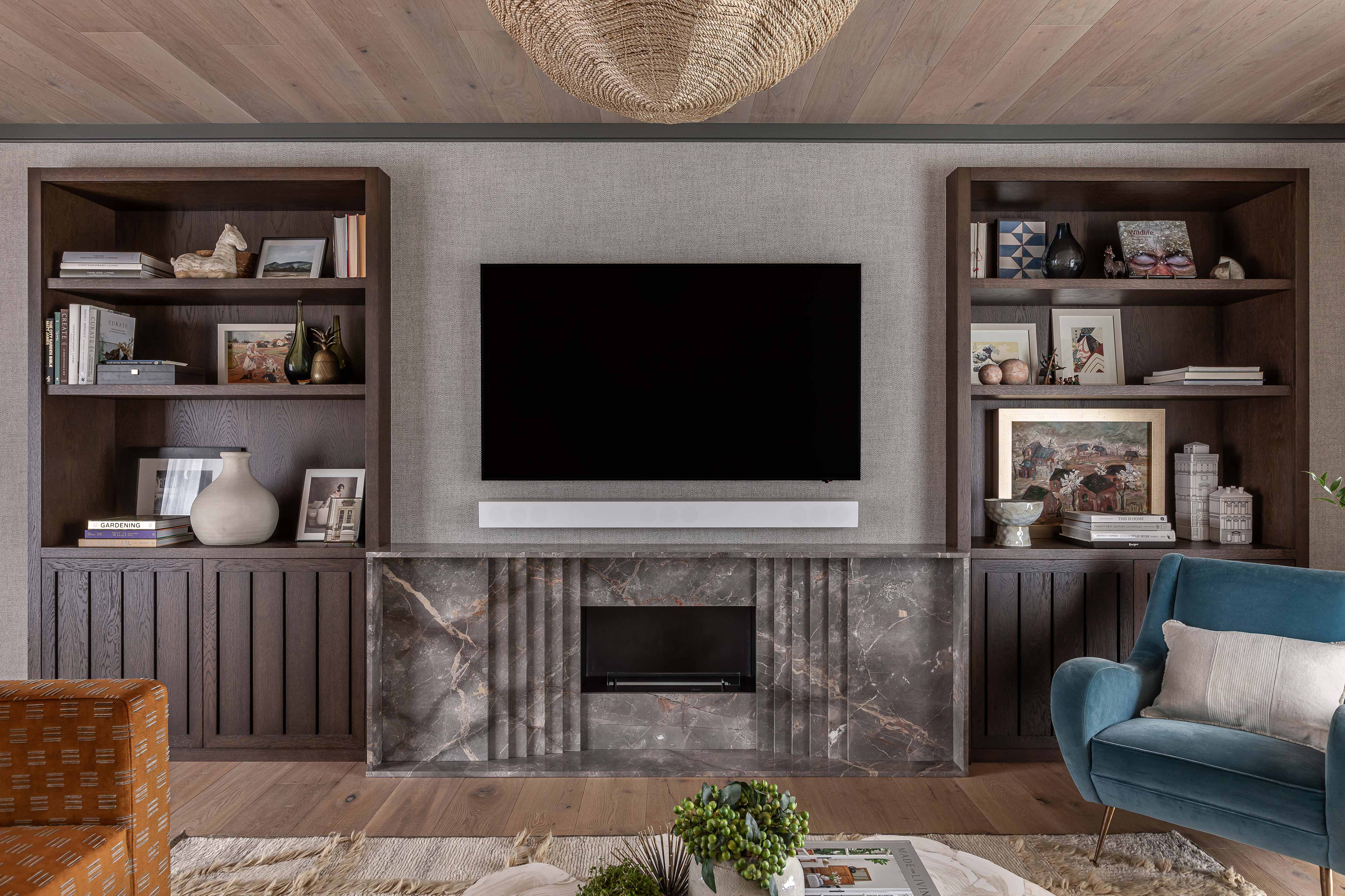Dark stained oak bespoke joinery flanking the fireplace with vertically slatted storage cupboards and open shelving, all by Origins Design for Chantel Elshout. 