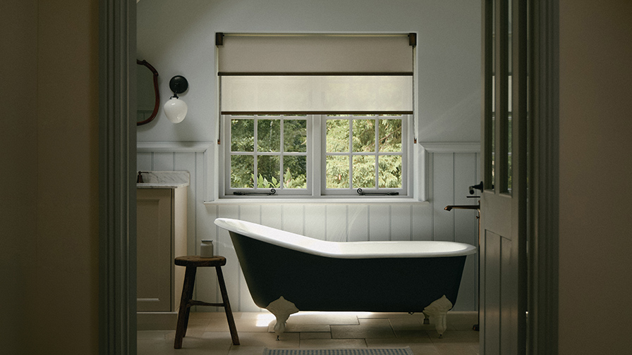 Cotswolds heritage bathroom featuring VENESTRE double roller blind with two fabrics, custom-fitted to original windows above a freestanding bathtub. The window treatments preserve architectural character while providing privacy and diffused natural light.