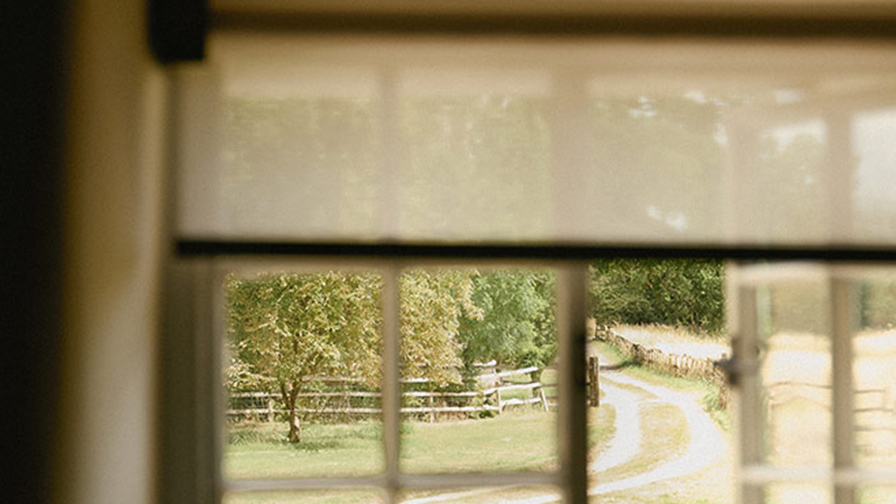 Close-up view through a VENESTRE sheer roller blind fabric, highlighting its delicate texture and soft light-filtering qualities within a countryside home.