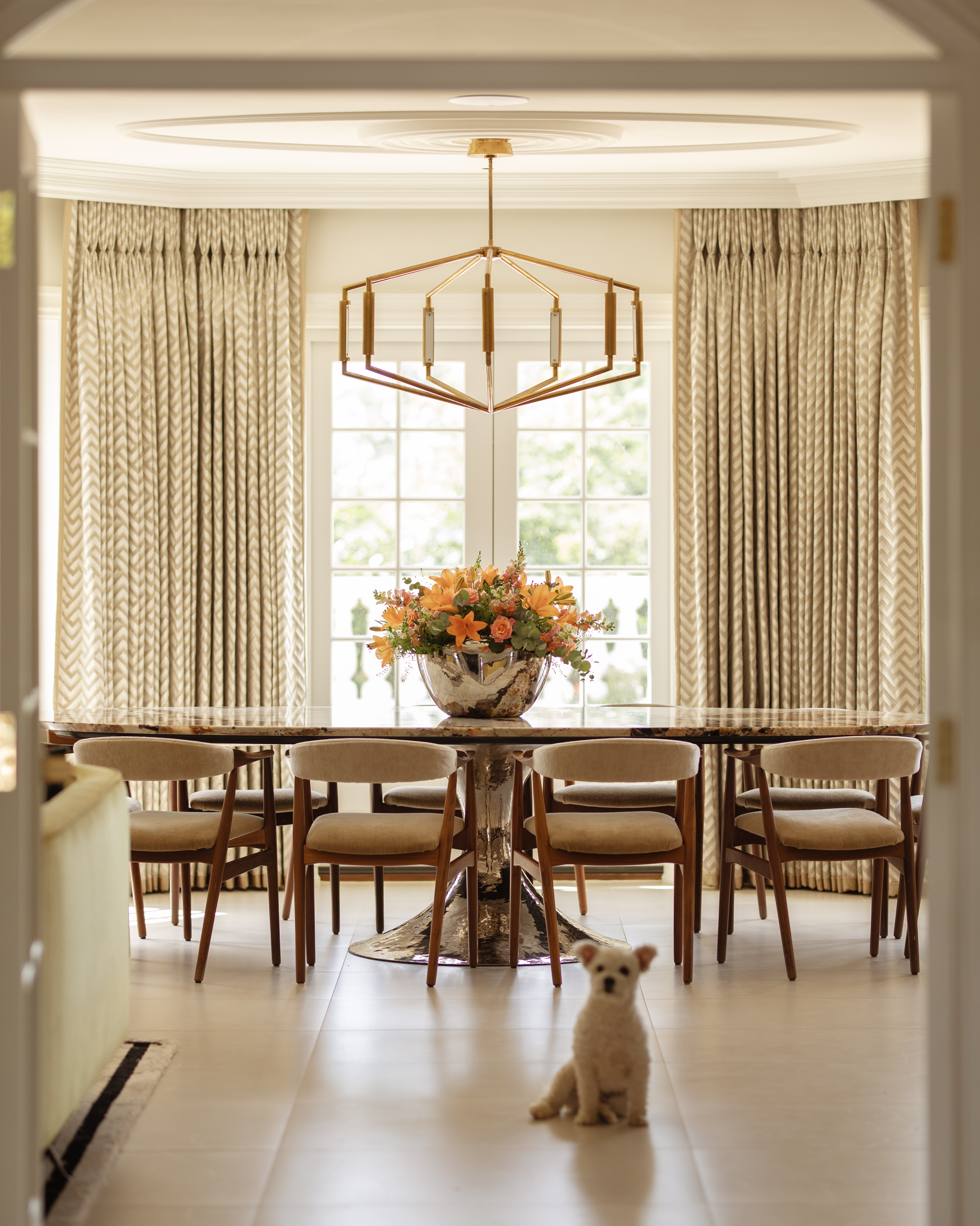 Dining table and chairs with dramatic pendant light above and view to gardens beyond