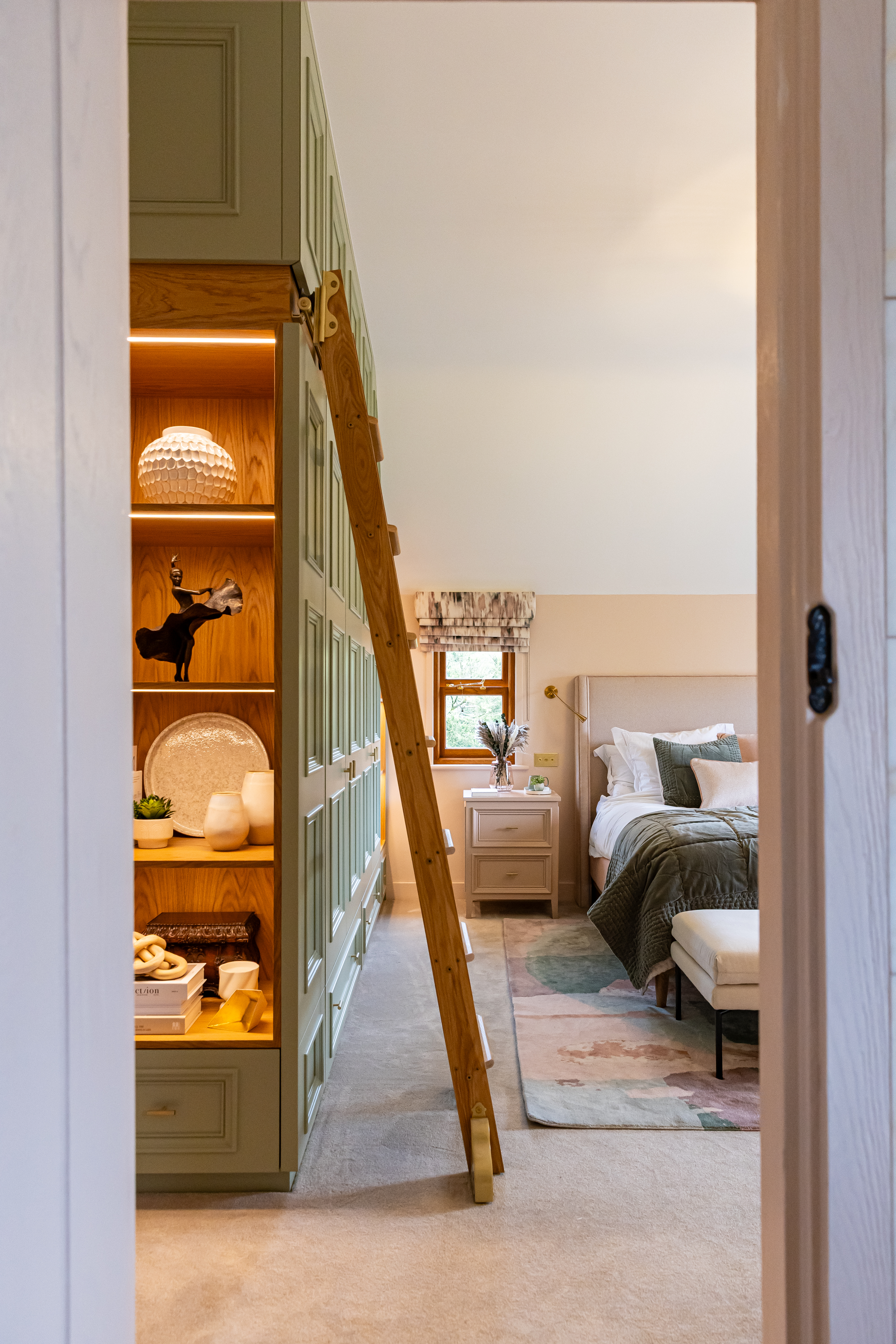 Bespoke wardrobes with illuminated display shelving at either end and library ladder to access the top cupboards