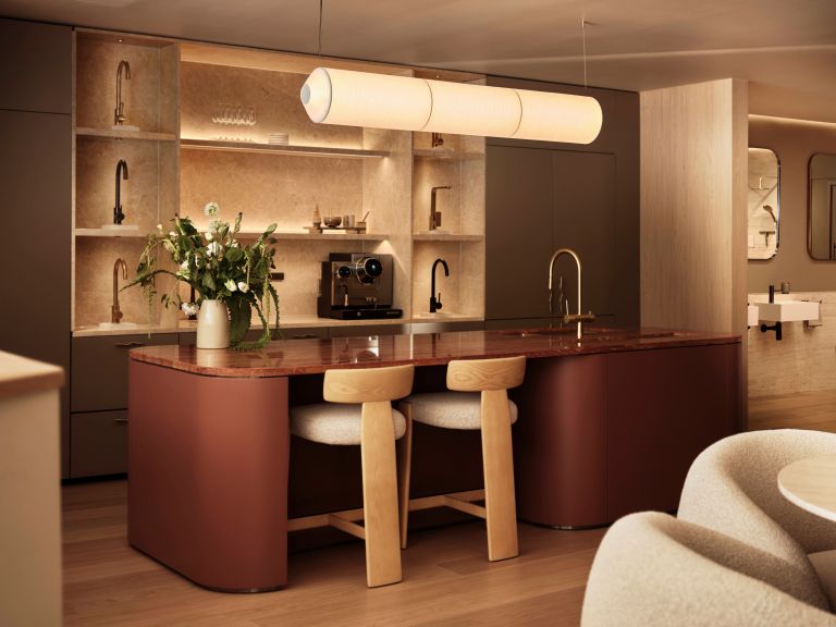 Neutral coloured kitchen set up with 2 bar stools, a kitchen island and a cream horizantal light.