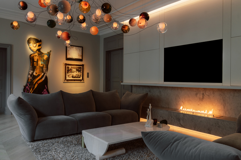 A front room with ball lights hanging from the ceiling, a wall-mounted T and grey sofas